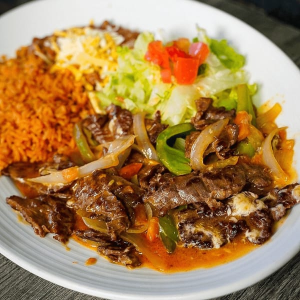 Las Salsas Taqueria's steak fajitas with rice, beans, lettuce, and tomatoes on a white plate.