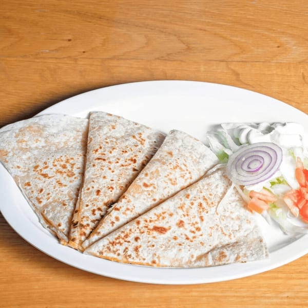 Four folded quesadillas with a side of lettuce, diced tomatoes, sour cream, and red onion.