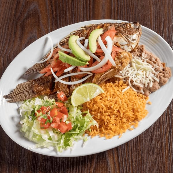 Whole fried tilapia with avocado, tomato, onion, rice, beans, and salad on a white plate.