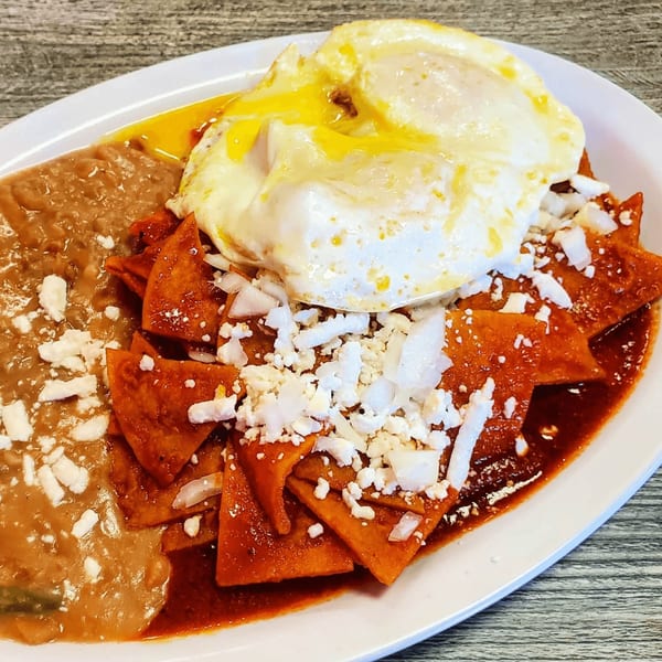 Chilaquiles with two fried eggs, refried beans, and crumbled cheese on a white plate.