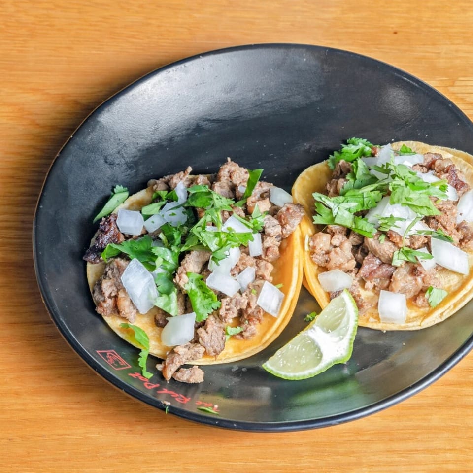 Two Las Salsas Taqueria carne asada tacos with onions, cilantro, and a lime wedge.