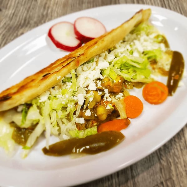 A Mexican gordita filled with meat, lettuce, and cheese, served with radishes and carrots.