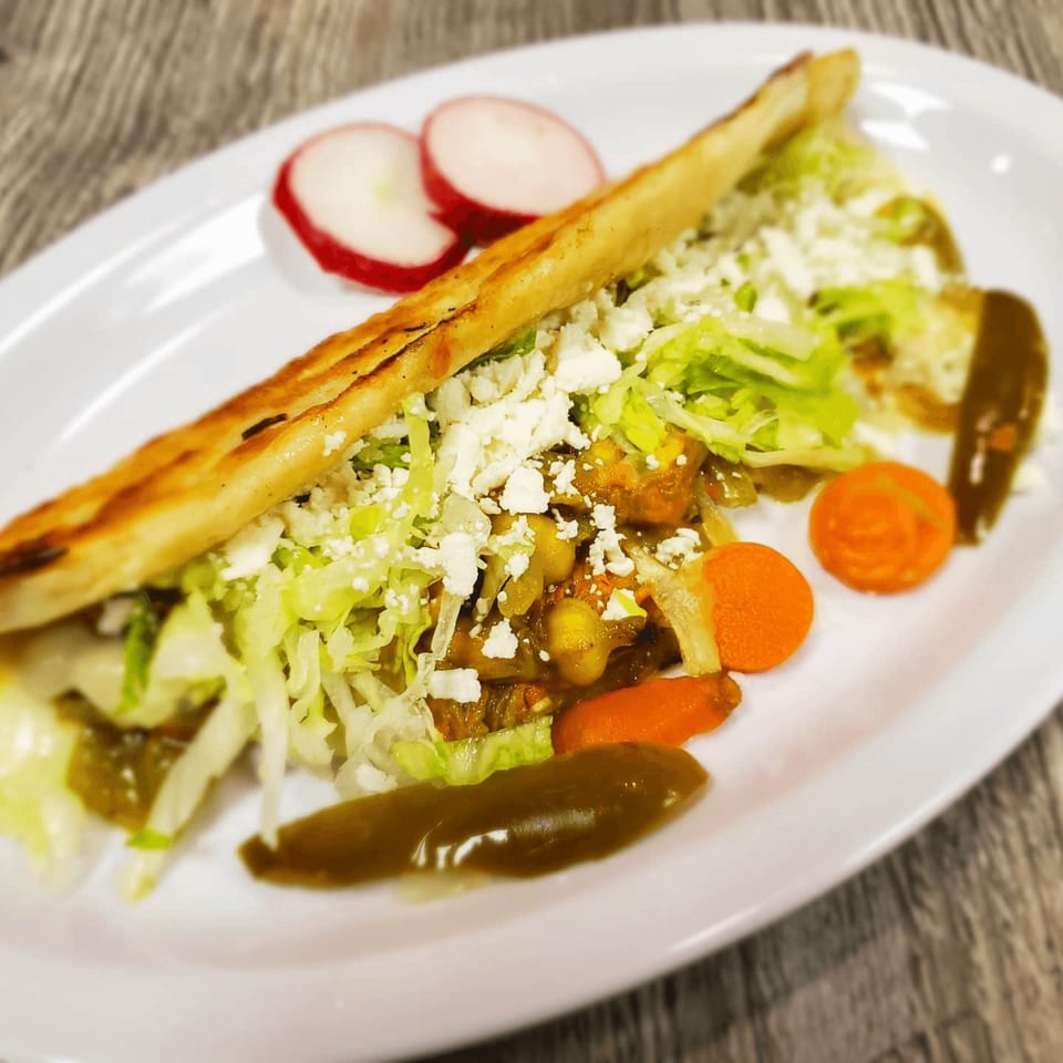 A Mexican gordita filled with meat, lettuce, and cheese, served with radishes and carrots.