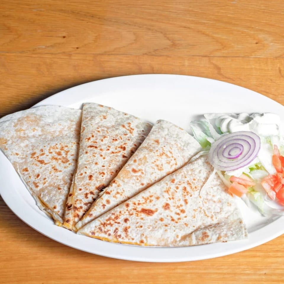 Four quesadilla wedges with a side of lettuce, diced tomatoes, red onion, and sour cream.
